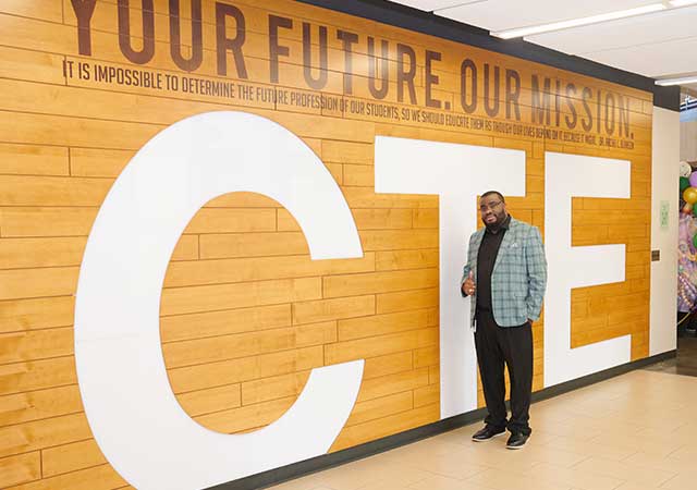 CTE Wall Mr. Bingham A man in a green plaid jacket stands in front of a large CTE sign with the quote Your Future. Our Mission.