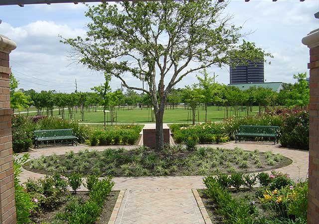 A landscaped garden plaza at City View Park features a central tree, brick pathways, benches, and neatly arranged plants with open park space beyond.