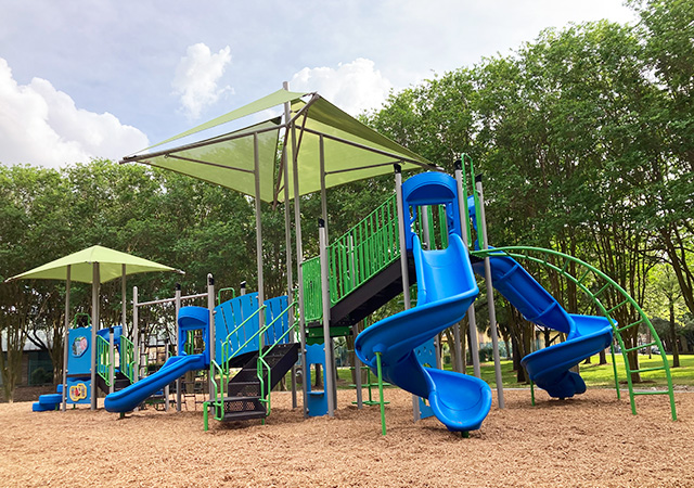Colorful playground structure at City View Park featuring blue slides, climbing areas, and shaded canopies surrounded by trees and mulch surfacing.