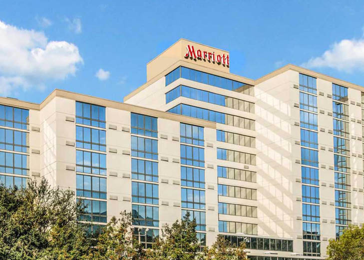Marriott 350x250 A bright daytime photo of the Houston Marriott North hotel featuring its modern glass windows, cream-colored exterior, and blue sky with scattered clouds overhead.