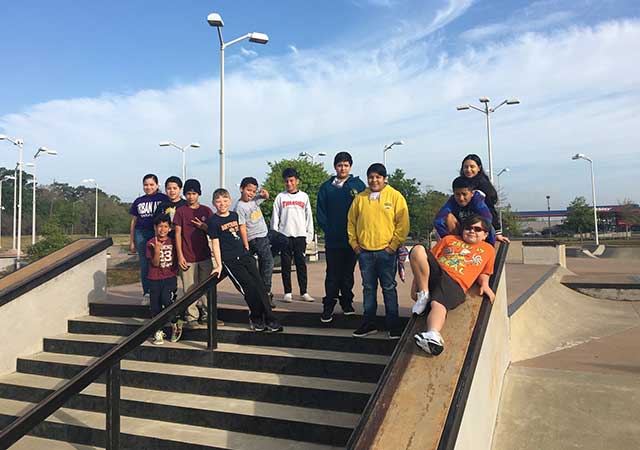 A group of children pose together on concrete steps and ramps at the North Houston Skate Park, smiling and gathering for a group photo during a community skate event.