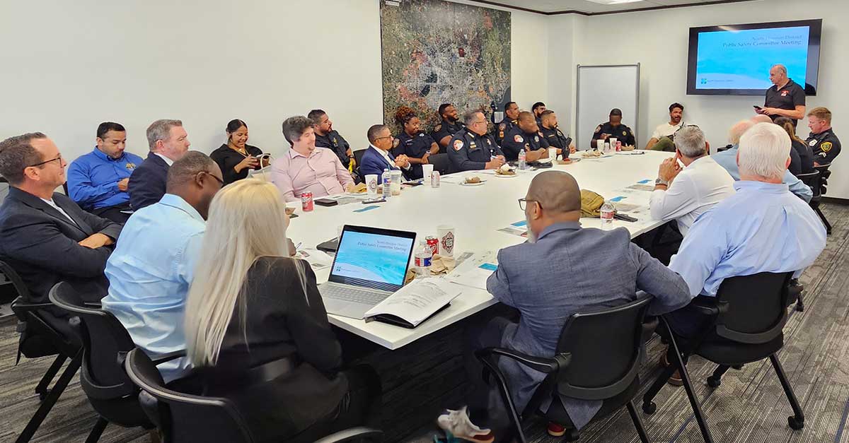 Attendees seated around a large conference table at the North Houston District Public Safety Committee Meeting, with a presentation screen at the front of the room.