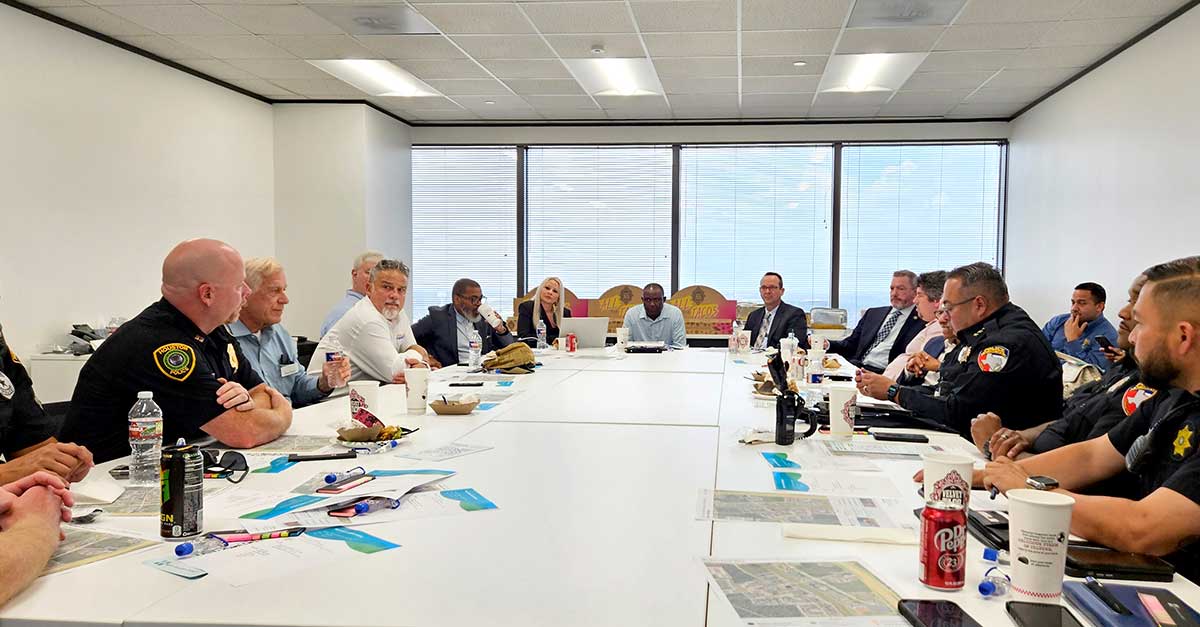 Participants from multiple public safety agencies seated around a conference table during a meeting in a room with large windows and natural light.