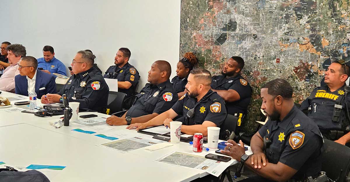 Sheriff’s deputies and local officials attentively listen during a public safety meeting, seated in front of a large wall map.