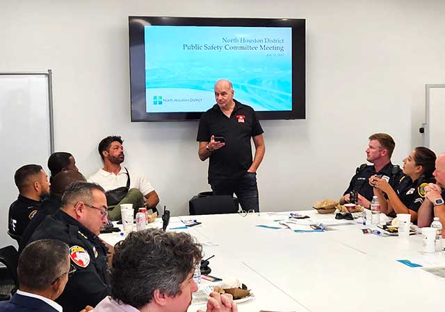 A man stands and addresses the group during the North Houston District Public Safety Committee Meeting, with a title slide projected behind him.