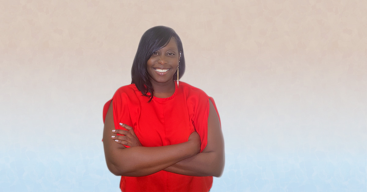 Portrait of Sheena Childs smiling with arms crossed while wearing a red blouse against a light neutral background.