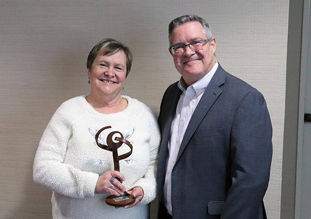 A woman holds a modern sculpture award while smiling next to a man in a gray blazer, celebrating her 10-year service milestone.