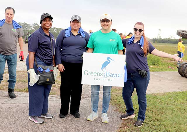 Tina Poindexter GBC Tree Planting Tina Poindexter stands with four other volunteers outdoors holding a Greens Bayou Coalition sign at a community event, all dressed casually and smiling for the photo.