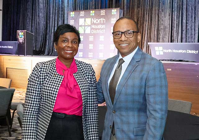 Tina Poindexter PS Awards 2024 Tina Poindexter and a man in a blue plaid suit stand smiling in front of a stage with North Houston District signage and podiums in the background.